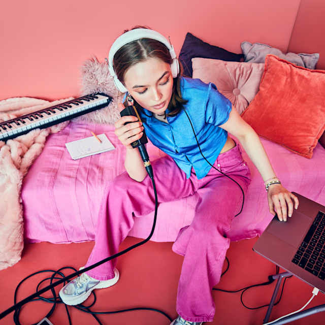A girl in her bedroom recording vocals with a microphone on her laptop