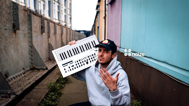Noize London in front of a building holding a music instrument