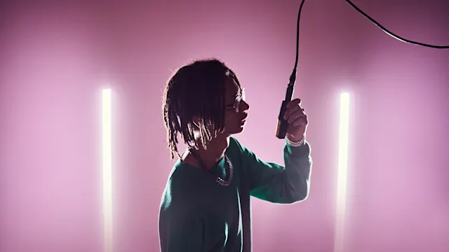 A vocalist holding a mic hanging from the ceiling in a pink room