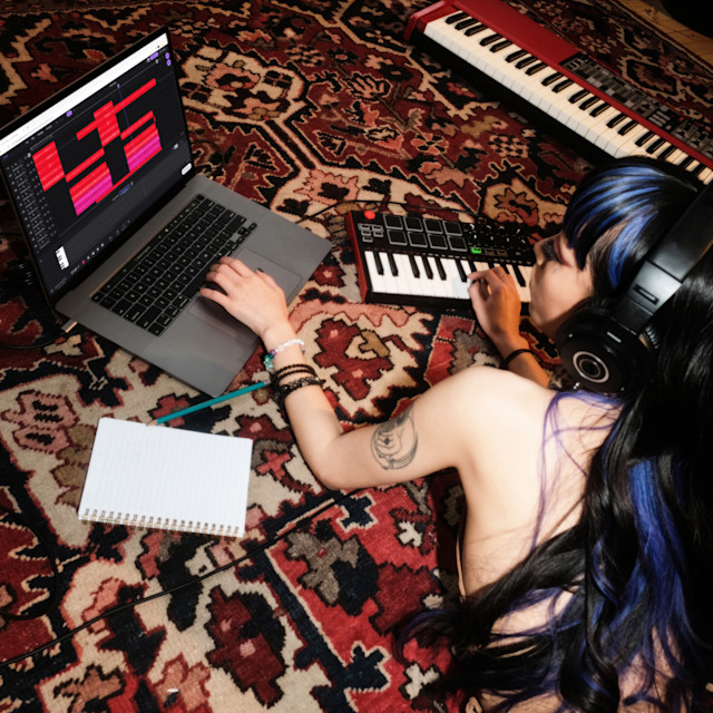 A woman on the floor recording piano on her MIDI controller.