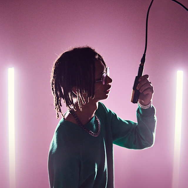 Male vocalist holding a mic hanging from the ceiling in a pink room