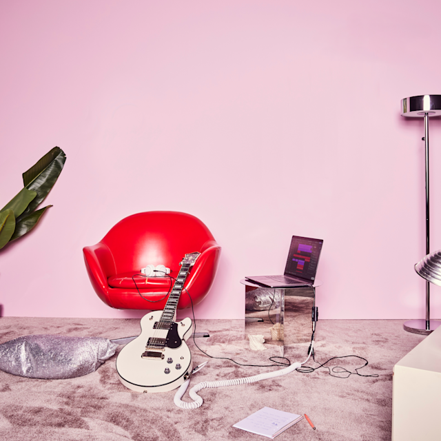 A room with a guitar leaning on a chair next to a laptop